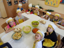 dzieci ubrane w fartuszki i czapki kucharskie, kroją warzywa