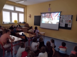 uczniowie ubrani w fartuszki jedzą chleb, oglądają film